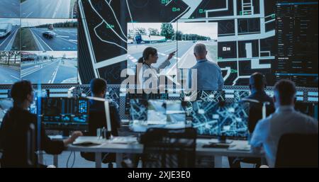 Team of Software Developers, Engineers and Data Scientists Working in a Modern Logistics Technology Company. Male and Female Having a Discussion in Front of a Screen with Surveillance CCTV Footage Stock Photo