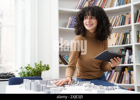 Woman architect using tablet at library table while creating city workout Stock Photo