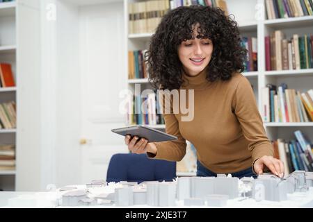 Female architect with city layout using digital tablet at library table with books in background Stock Photo