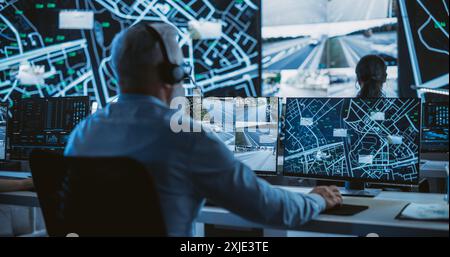 Senior Specialist in a Dark High-Tech Monitoring Room, Concentrated on a Call and Computer Work. Fleet Manager Using Headphones with Built-In Mic for Communication with Delivery Vehicles Stock Photo