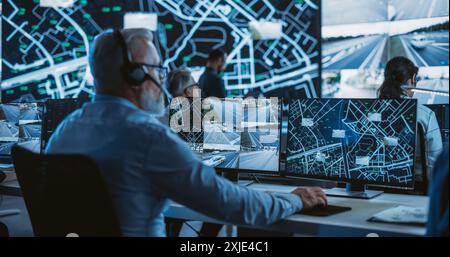 Technical Customer Support Specialist is Talking on a Headset while Working on a Computer in a Call Center Control Room Filled Display Screens with Monitoring Software. Over the Shoulder Footage Stock Photo
