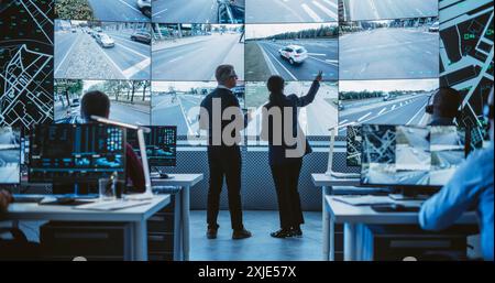 Two Diverse Male and Female Software Engineers Discuss Live Analysis Feed with City Road and Traffic Updates. Managers and Data Scientists Collaborate in a Modern Monitoring Office Stock Photo