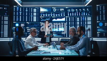 Diverse Team Of Data Scientists and Software Developers Discussing Reports in Monitoring Room with Analytics Feed on Big Digital Screen. Female Leading Artificial Intelligence Company Board Meeting Stock Photo
