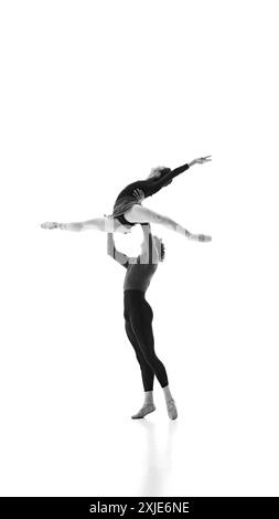 Dynamic duo in ballet training, focused on every move against white studio background. Black and white filter. Stock Photo