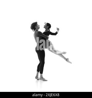 Duo's elegant ballet training session. Focused and poised dancers in motion against white studio background. Black and white filter. Stock Photo
