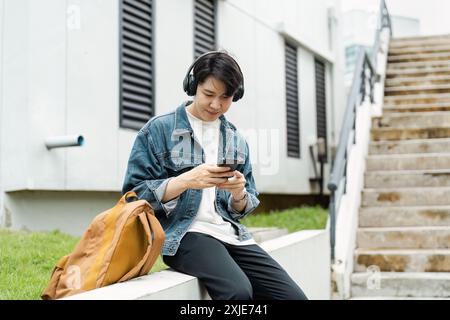 Young Man Listening to Music on Headphones While Using Smartphone Outdoors Near Urban City Stock Photo