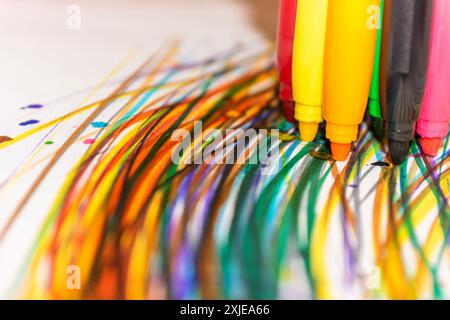 Multi-colored felt-tip pens draw multi-colored lines on a white sheet of paper. Selective focus. Shallow depth of field. Creation. Abstraction. Stock Photo