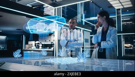 Male And Female Industrial Engineers Using Futuristic Technology Of Hologram of Wind Turbine Prototype In Computer Powered Laboratory. Multiethnic Colleagues Discussing a High-Tech VFX Projection. Stock Photo