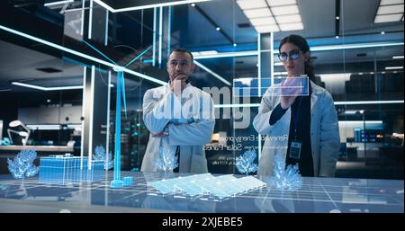 Male And Female Industrial Engineers Using Futuristic Hologram of Wind Turbine Prototype In Computer Powered Laboratory. Multiethnic Colleagues Controlling VFX Projection With Gestures. Stock Photo