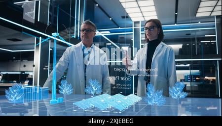 Male And Female Renewable Energy Engineers Using Futuristic Hologram of Wind Turbine Prototype In Computer Powered Laboratory. Caucasian Colleagues Controlling VFX Projection With Gestures. Stock Photo