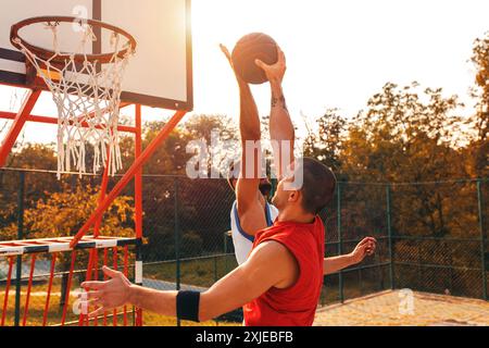 Two male friends playing basketball on court outdoors. Stock Photo