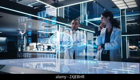 Two Neuroscientists Working With Computer-Powered VFX Hologram Of Human Brain And Nervous System In Modern Laboratory. Multiethnic Man And Woman Working On Technological Solutions for Brain Tumor. Stock Photo