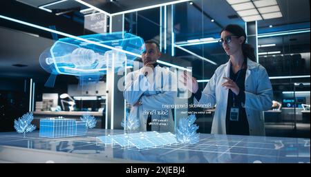 Male And Female Industrial Engineers Using Futuristic Hologram of Wind Turbine Prototype In Computer Powered Modern Laboratory. Multiethnic Colleagues Looking At High-Tech VFX Projection. Stock Photo