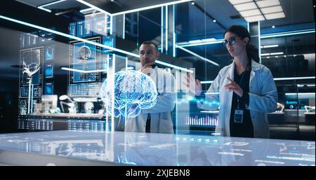 Two Neuroscientists Working With Computer-Powered VFX Hologram Of Human Brain And Nervous System In Futuristic Laboratory. Multiethnic Man And Woman Working On Technological Solutions for Brain Tumor. Stock Photo