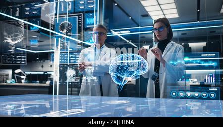 Two Neuroscientists Working With Computer-Powered VFX Hologram Of Human Brain And Nervous System In Futuristic Laboratory. Caucasian Man And Woman Working On Solutions for Brain Damage. Stock Photo