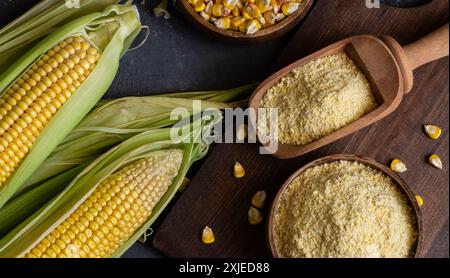 Corn flour in wooden bowl or spoon with fresh corn cobs, kernels on rustic table Stock Photo