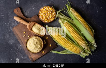Corn flour in wooden bowl or spoon with fresh corn cobs, kernels on rustic table Stock Photo