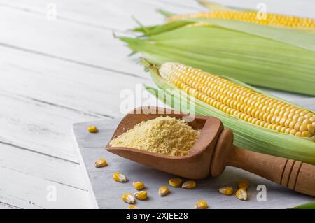 Corn flour in wooden bowl or spoon with fresh corn cobs, kernels on rustic table Stock Photo