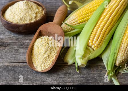 Corn flour in wooden bowl or spoon with fresh corn cobs, kernels on rustic table Stock Photo