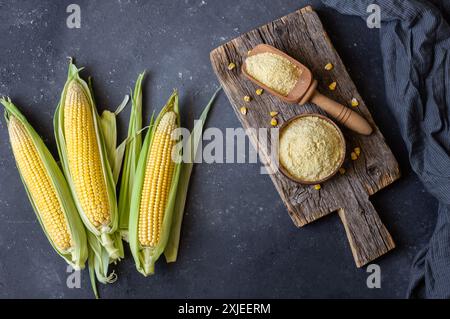 Corn flour in wooden bowl or spoon with fresh corn cobs, kernels on rustic table Stock Photo