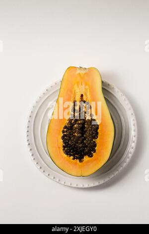 Half of a beautiful juicy ripe papaya on a white plate on a white table, top view Stock Photo