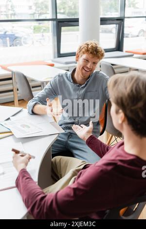 Two diligent male students engrossed in deep discussion at a library table. Stock Photo