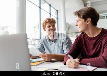 Two young men sitting at a table, focused on studying together using a laptop. Stock Photo