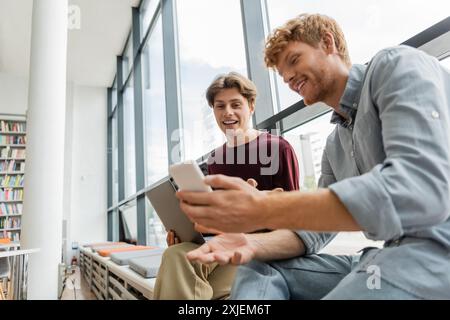 Two male students engage with a tablet while seated on the floor. Stock Photo