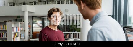 Two young male students discussing amidst shelves of books. Stock Photo