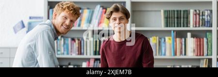 Two male students immersed in study, standing by a bookshelf. Stock Photo