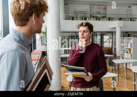 Two male students engage in deep study amidst towering shelves of books. Stock Photo