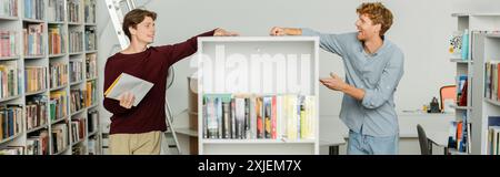 Two young students exploring books in library. Stock Photo