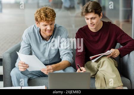 Two men engrossed in laptop work on couch. Stock Photo