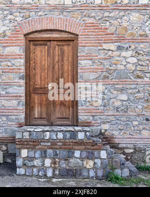A stone building with a wooden double door and stone steps leading up to it. The door has a simple brass handle. The stonework is a mix of rough-hewn and brick, creating a textured appearance. Stock Photo