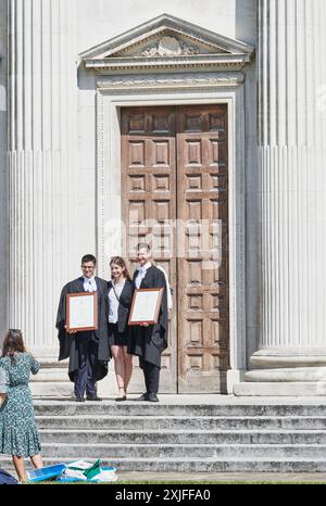 A couple of students, in academic dress, fromTrinity College, University of Cambridge, England, proudly hold certificates after their degree award ceremony in Senate House on 18 July 2024 Stock Photo