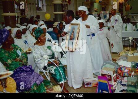 Harvest festival church service, the Celestial Church of Christ London. A pastor walks amongst his congregation with an Image of Christ. Toys for children are on the floor as part of the ‘harvest’. 1993 England. 1990s UK HOMER SYKES Stock Photo