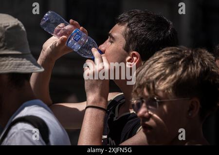 A young man seen drinking water to combat the heat while waiting to visit a unique building representative of Catalan modernism. The first heat wave of the summer presents warning notices in some regions of Spain. Temperatures above 40 degrees are expected in most regions of southern Spain. The city of Barcelona is already experiencing a sharp increase in heat, especially in open areas without shade. Stock Photo