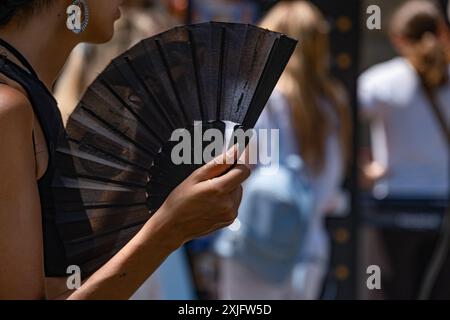 Barcelona, Catalonia, Spain. 18th July, 2024. A woman seen cooling herself with a fan to combat the heat of the city while waiting to visit a unique building representative of Catalan modernism. The first heat wave of the summer presents warning notices in some regions of Spain. Temperatures above 40 degrees are expected in most regions of southern Spain. The city of Barcelona is already experiencing a sharp increase in heat, especially in open areas without shade. (Credit Image: © Paco Freire/SOPA Images via ZUMA Press Wire) EDITORIAL USAGE ONLY! Not for Commercial USAGE! Stock Photo