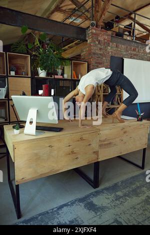 Sportive woman, office employee standing on her desk and doing stretching exercises. Fusion of fitness and productivity Stock Photo