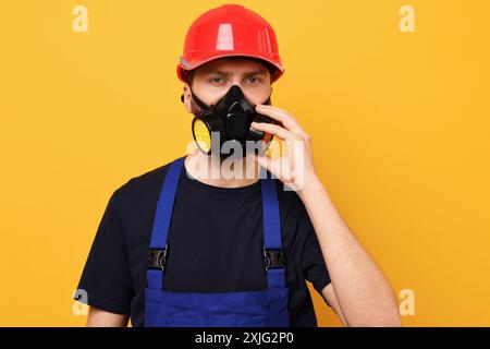 Man in respirator mask and hard hat on yellow background Stock Photo