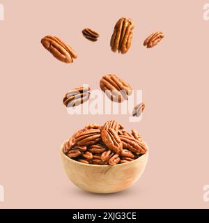 Pecan nuts falling into bowl on beige background Stock Photo