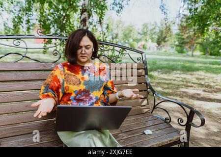 Female professional enjoys remote video conferencing on a calm sunny day in green park. Casual Asian businesswoman, smiles as she successfully multita Stock Photo