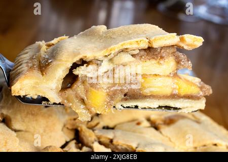 Making of an apple pie:  Cutting the pie.  Using a pie server to lift the first piece of pie from the pie plate. Stock Photo