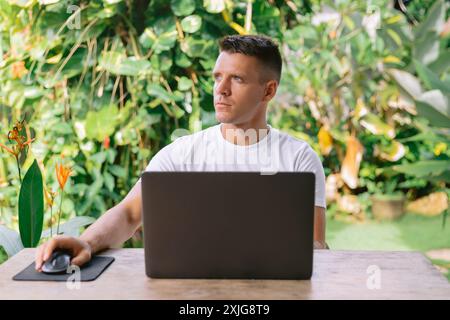 Focused young man thinking about new idea with laptop, successful freelancer working online on computer in summer cafe Stock Photo