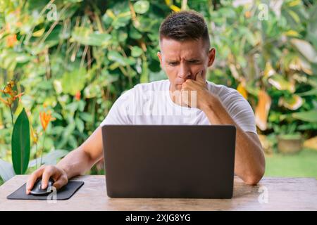 Serious man using laptop, successful freelancer working online on computer sitting in outdoor kitchen Stock Photo