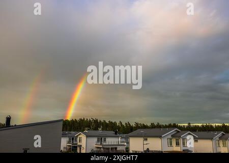 Beautiful view of double rainbow in sky with clouds after rain, over villa community and pine trees. Sweden. Stock Photo