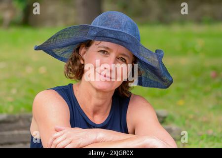 portrait of a romantic elderly woman 50-55 years old in a blue lady's hat on the background of a summer garden Stock Photo