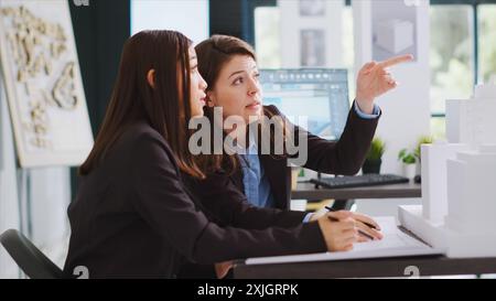 Developers trying to design blueprints for new construction site, working together to draw lines and create architectural drafts for project. Technicians examine 3d printed models at workstation. Stock Photo