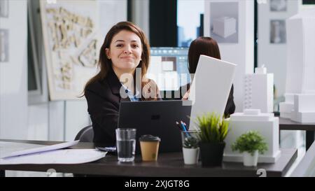 Portrait of architect examines 3d model scale to gather dimensions and create industrial blueprint for property remodeling project. Cad specialist working on engineering plan. Handheld shot. Stock Photo