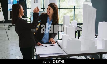 Designing staff gives high five upon achieving success on their restoration task, architectural agency workers coordinate to carry out manufacturing plans. CAD specialists develop draft schemes. Stock Photo